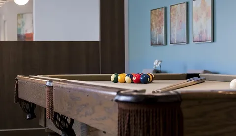 Pool table with coloured balls and cues beneath abstract wall art