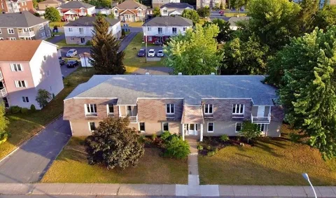 Aerial view of a low-rise residence with a lawn, front path and trees