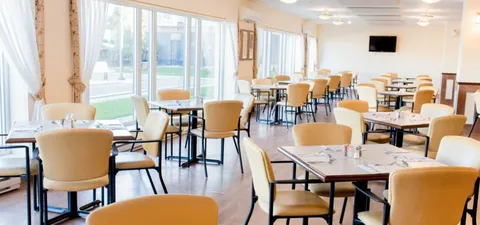 Dining room with tables and chairs beside large windows.