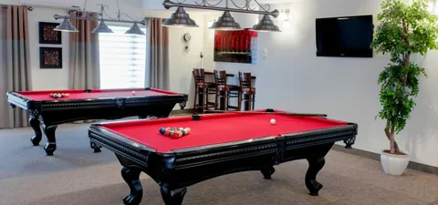 Two billiards tables beneath pendant lights beside a wall television.