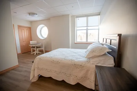 Suite bedroom with a double bed, bedside table and large window.