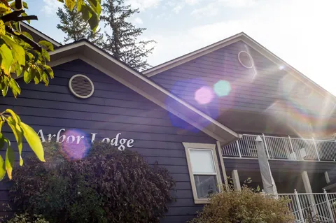 Grey building with gabled roofs, balconies, shrubs and an Arbor Lodge sign
