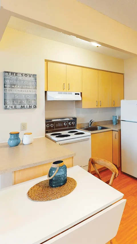 Kitchenette with yellow cupboards, appliances and a small dining table.