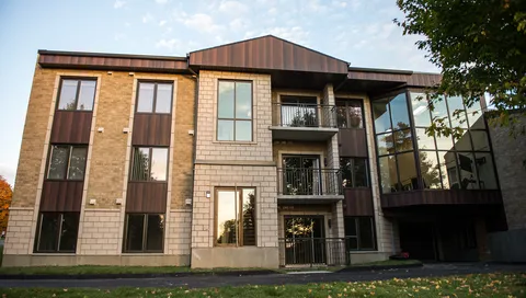 Brick residence with balconies, large windows and a paved driveway.