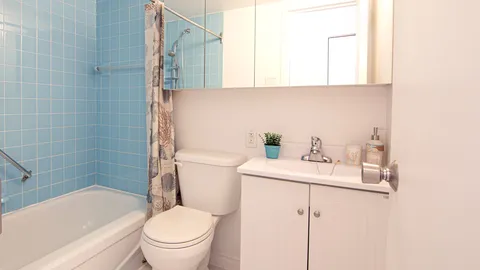 Suite bathroom with a toilet, sink cabinet and tiled bath area.