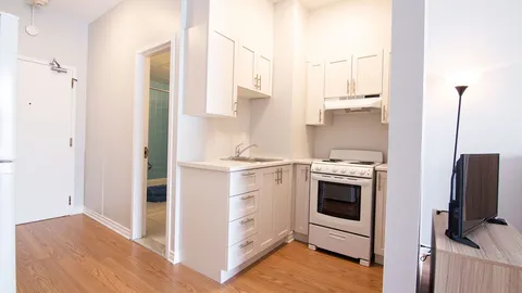Studio kitchenette with white cabinets, a stove and a sink.