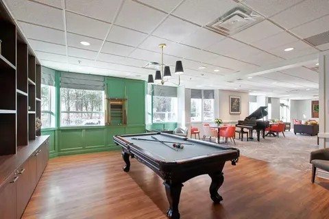 Room with a pool table, grand piano and red chairs