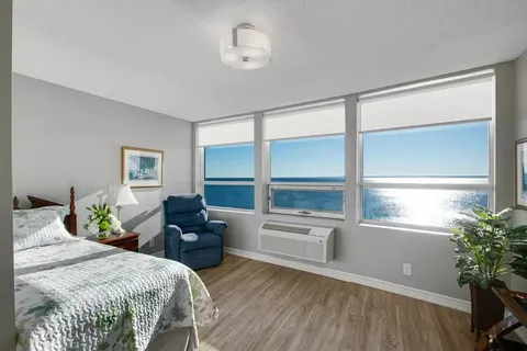 Bedroom with a bed, blue armchair and windows overlooking water