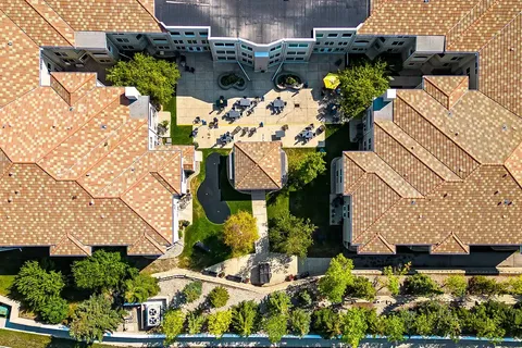 Aerial view of tiled roofs enclosing a courtyard with tables, paths and garden beds