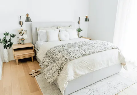 Bedroom with white bedding, wooden bedside tables and wall lamps