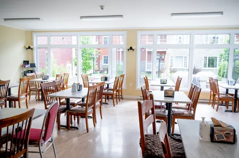 Dining room with wooden tables beside large windows.