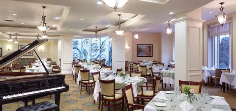 Dining room with a grand piano and tables beside large windows