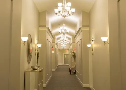 Corridor with wall lights, chandeliers and seating.