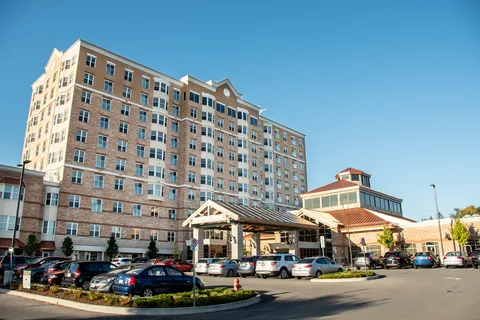 Residence tower and entrance canopy beyond parked cars and a driveway
