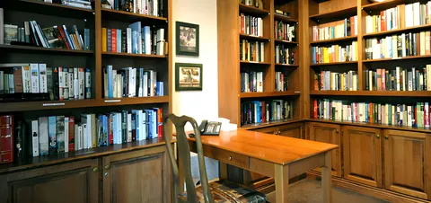 Library with wooden bookshelves, chairs and a reading table.