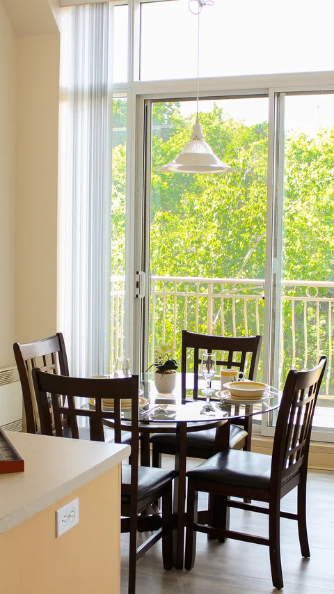 Dining table and wooden chairs beside a suite balcony window.