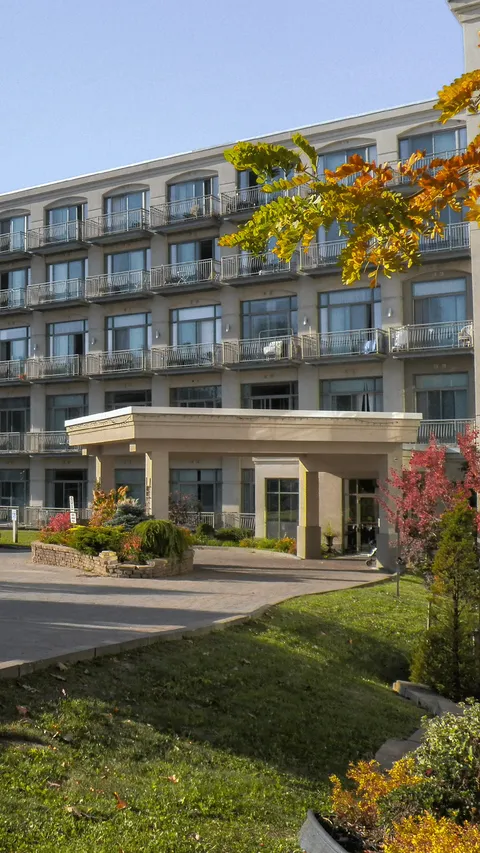 Residence facade with balconies and a covered entrance beside autumn trees.
