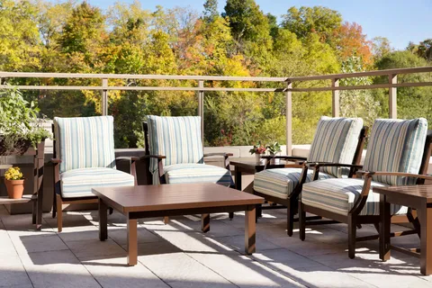 Outdoor terrace with wooden seating and trees beyond a glass railing.