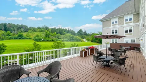Wooden deck with patio furniture and umbrellas beside a lawn