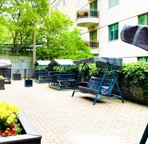 Paved courtyard with canopy swings, trees and flower planters beside the building