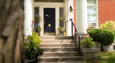 Front door reached by steps with a railing and potted plants.