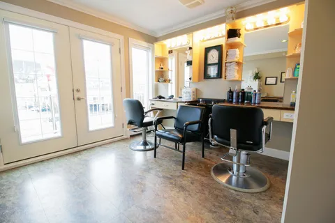 Salon chairs beneath mirrors beside glass doors