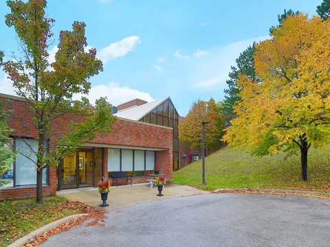 Brick building with an entrance beside trees and a paved driveway