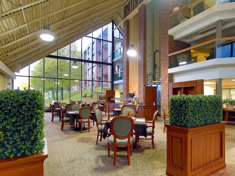 Dining area with tables and striped chairs beneath large windows and a high ceiling