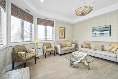 Armchairs and a sofa around a glass coffee table beside three windows