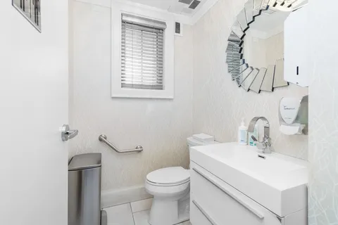 Bathroom with a toilet, white vanity, mirror and metal grab bars