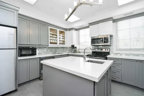 Grey kitchen cabinets, a white island and stainless steel appliances