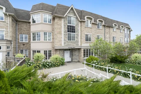Stone building with a central entrance, garden beds and white railings