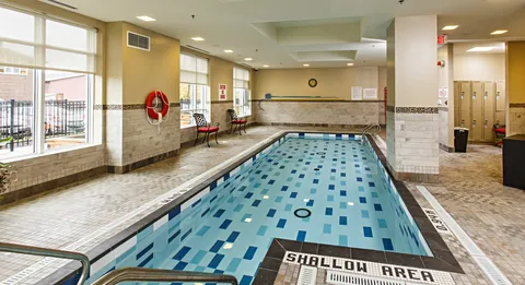 Indoor swimming pool with tiled walls, windows and poolside chairs
