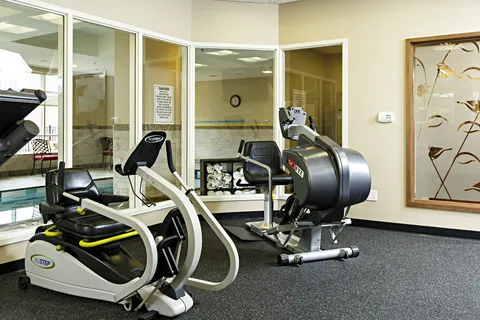 Fitness room with exercise machines beside windows overlooking a pool