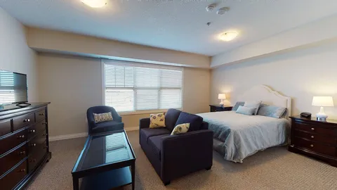 Studio suite with a bed, armchair, dresser and window.