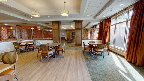 Dining room with round tables and windows along one wall.