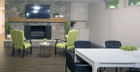 Two green armchairs beside a stone fireplace, television and side table