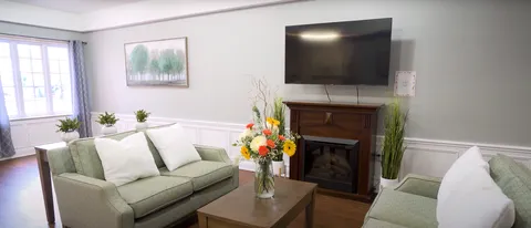 Lounge with green sofas, a fireplace, a black television and tall windows