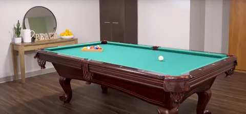 Billiard table beside a round mirror, a narrow table and wooden cabinets