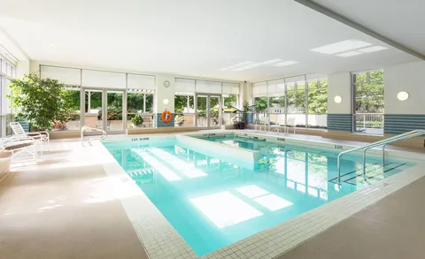 Indoor pool surrounded by seating and large windows.