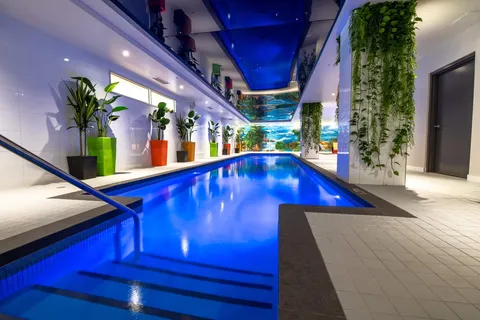 Indoor swimming pool with blue lighting, tropical murals and potted plants