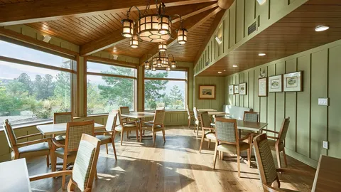 Window-side seating area with wood tables and chairs, chandeliers and framed landscapes.