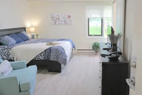 Bedroom with blue bedding, an armchair, a dresser and a window