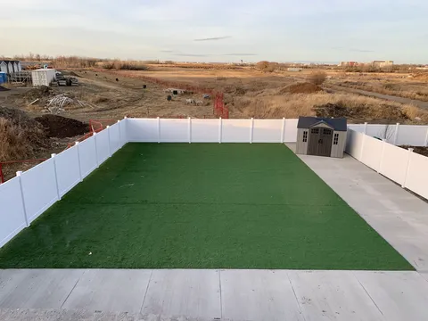 Fenced courtyard with artificial turf and raised planters.