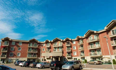 Red brick residential building with balconies, a covered entrance and parked cars