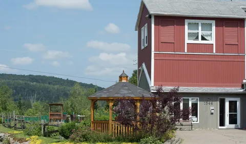 Red residence beside a wooden gazebo, flowerbeds and a paved entrance