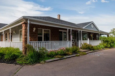 Low-rise building with a covered porch, white railings and planted beds