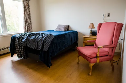 Bedroom with a blue-covered bed, a pink armchair and a bedside cabinet