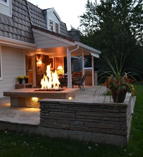 Outdoor fire pit with chairs on a landscaped patio.