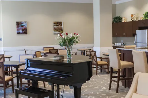 Common room with a piano, tables and a kitchen counter.
